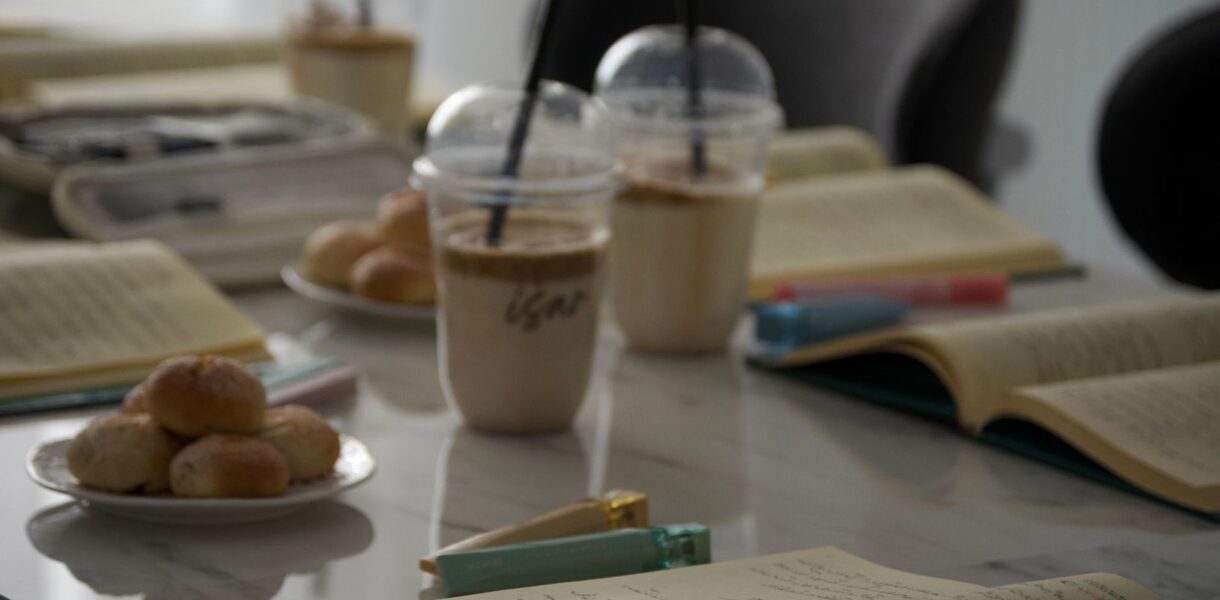 Öppna böcker, iskaffe och fika på ett bord.